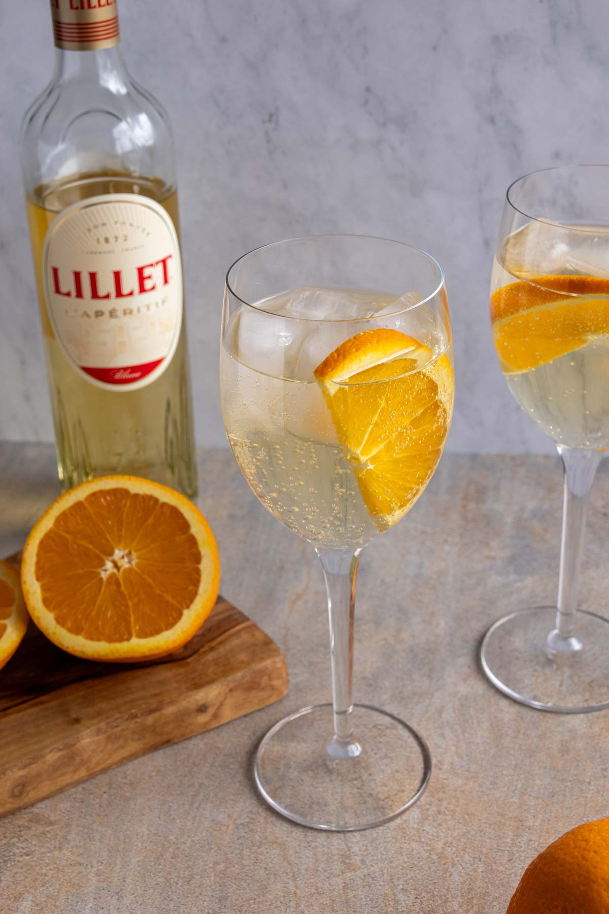 Two glasses of Lillet Spritz next to a wooden board with a halved orange on it.