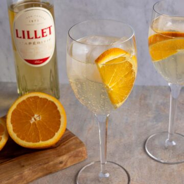 Two glasses of Lillet Spritz garnished with half orange slices.