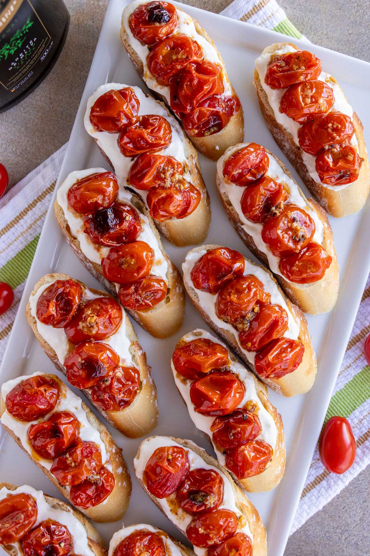 Stracciatella bruschetta with roasted cherry tomatoes arranged in two rows on a platter.