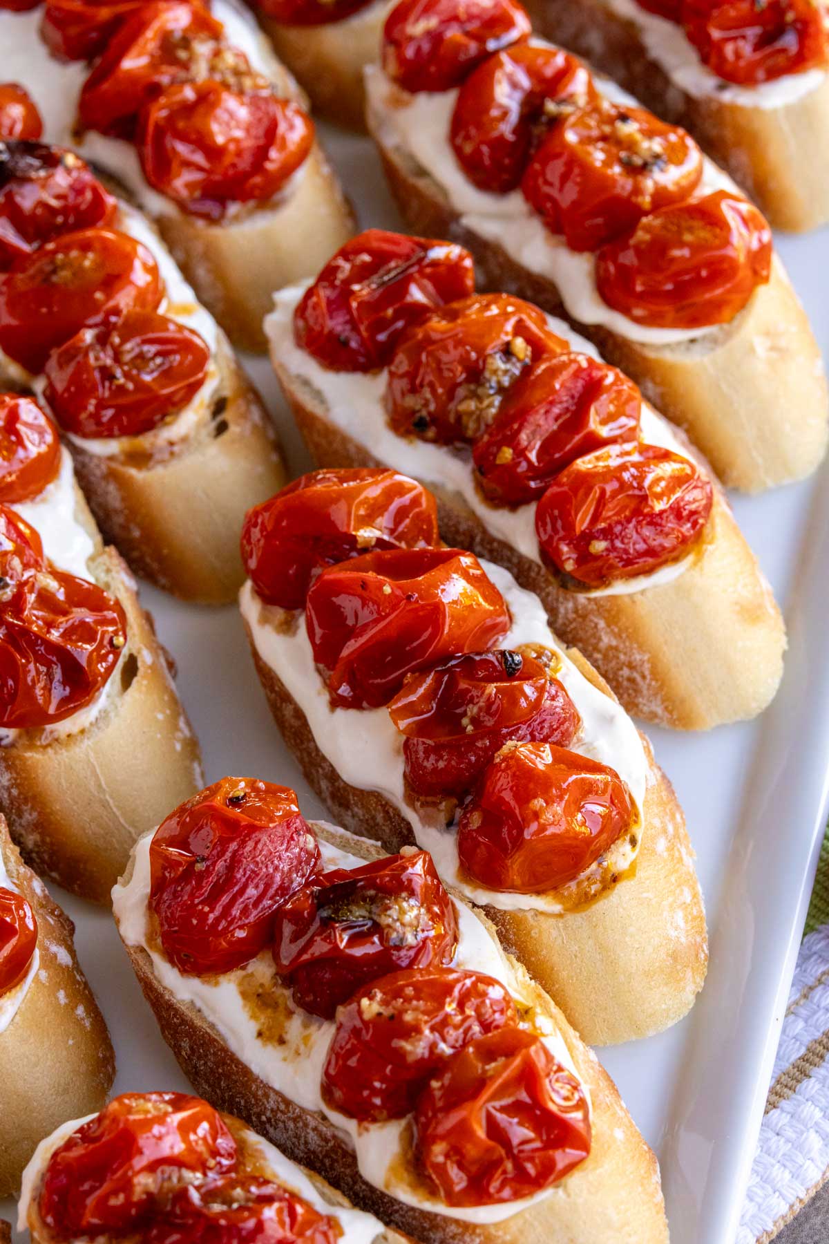 Bruschetta topped with stracciatella cheese and garlic-roasted cherry tomatoes arranged on a platter.