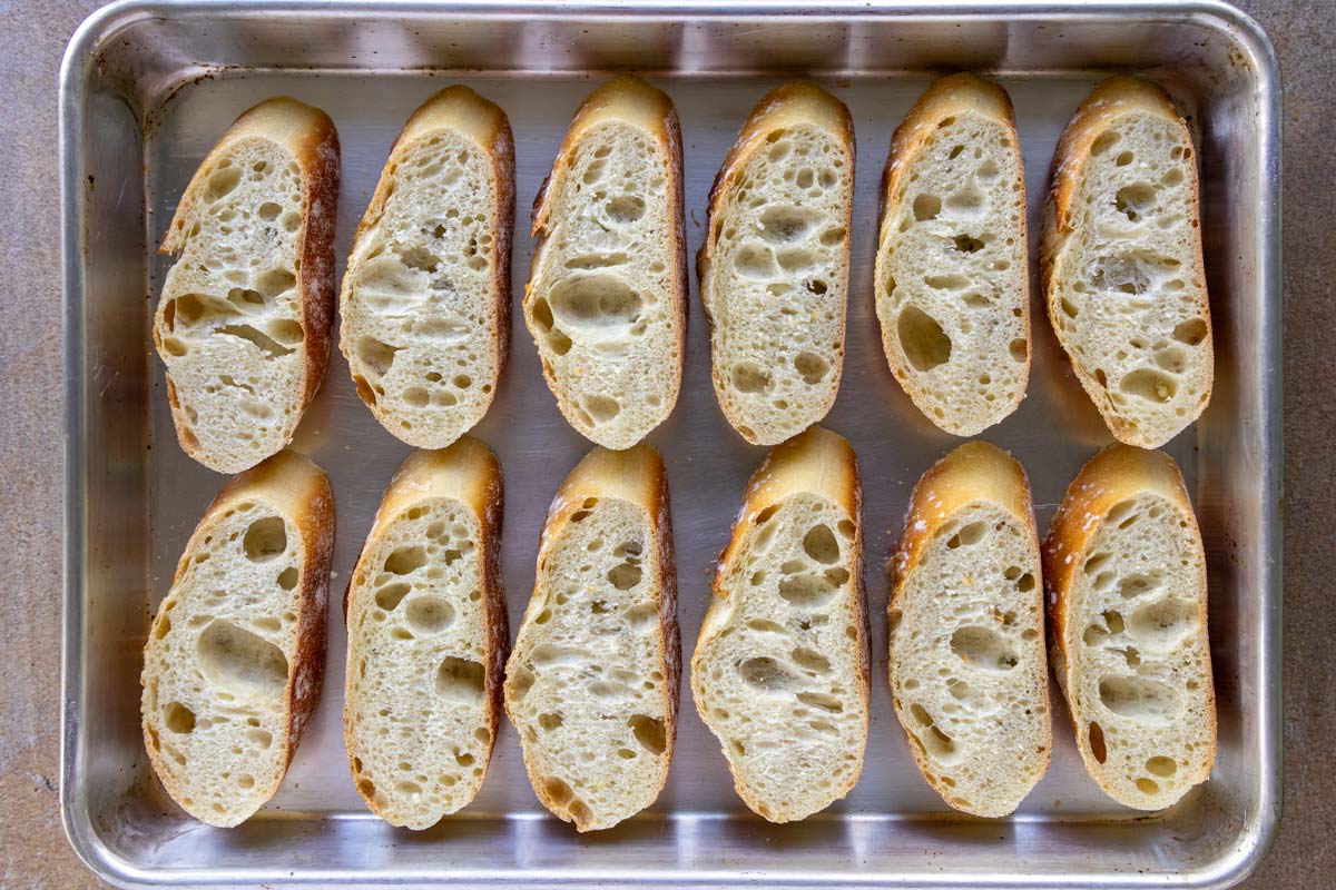Slices of lightly toasted baguette on a smalling baking sheet.