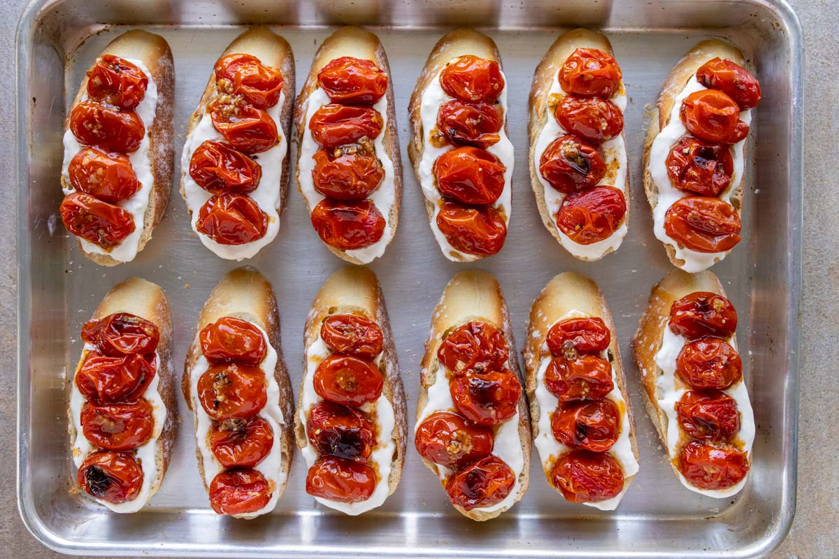 Stracciatella-topped slices of baguette finished with four roasted cherry tomatoes each.
