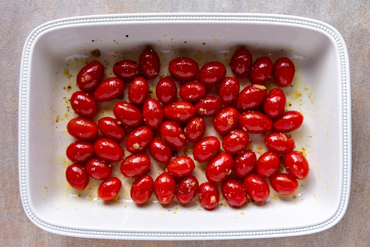 Cherry tomatoes mixed with garlic, olive oil, salt and pepper in a baking dish.