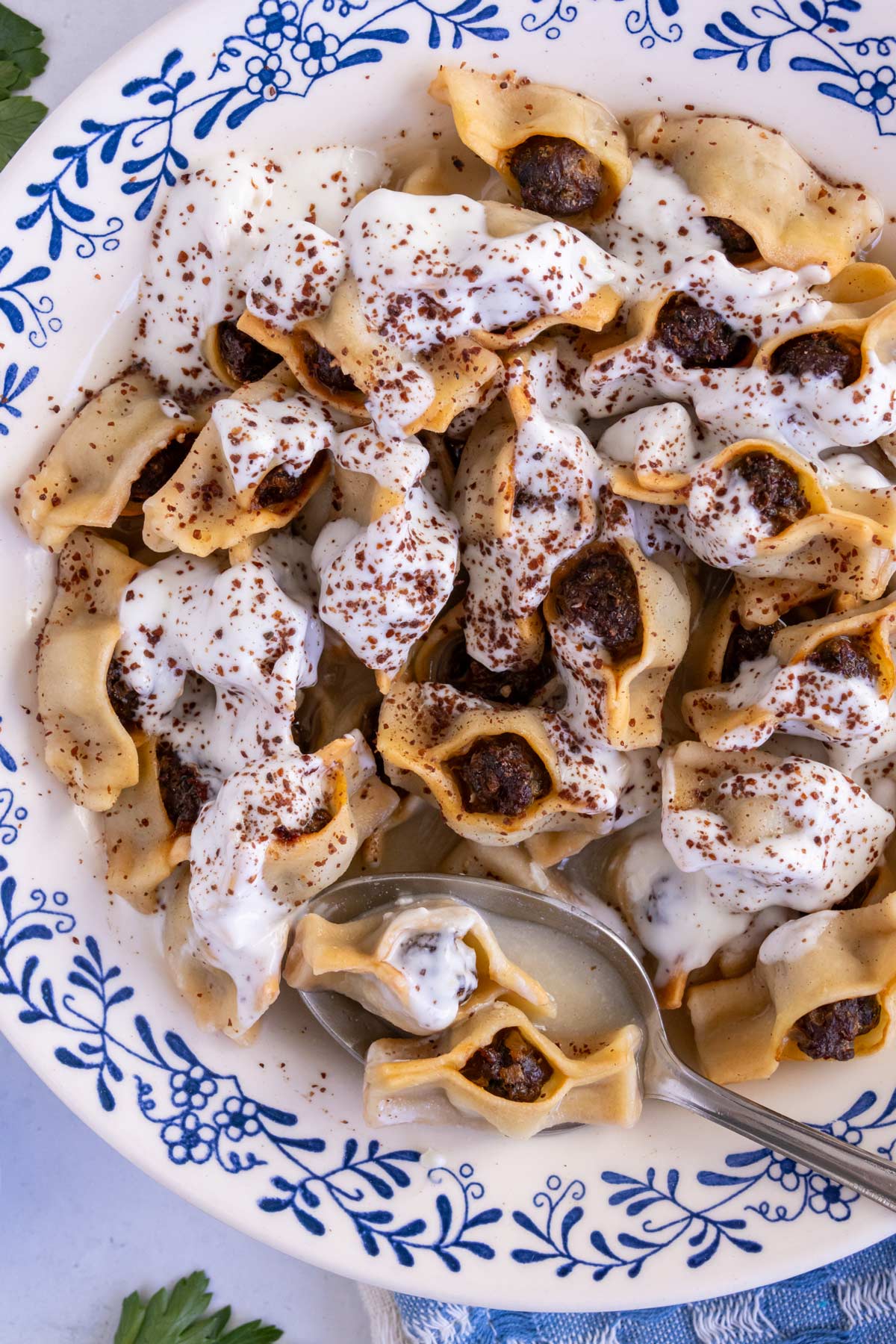 A spoon scooping a couple Armenian manti dumplings and broth out of a wide bowl.