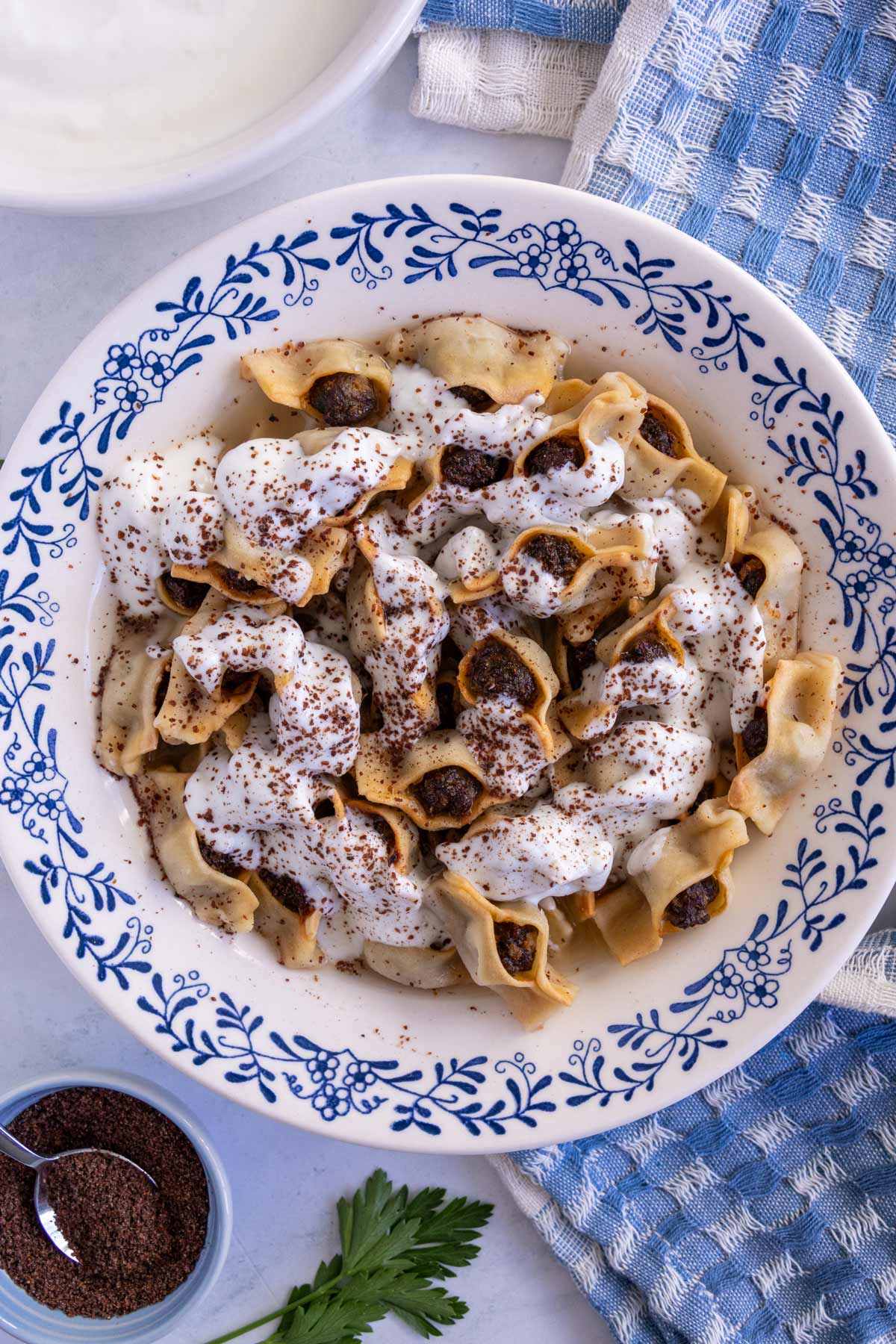 Armenian baked manti served in a wide bowl, topped with yogurt-garlic sauce and ground sumac.