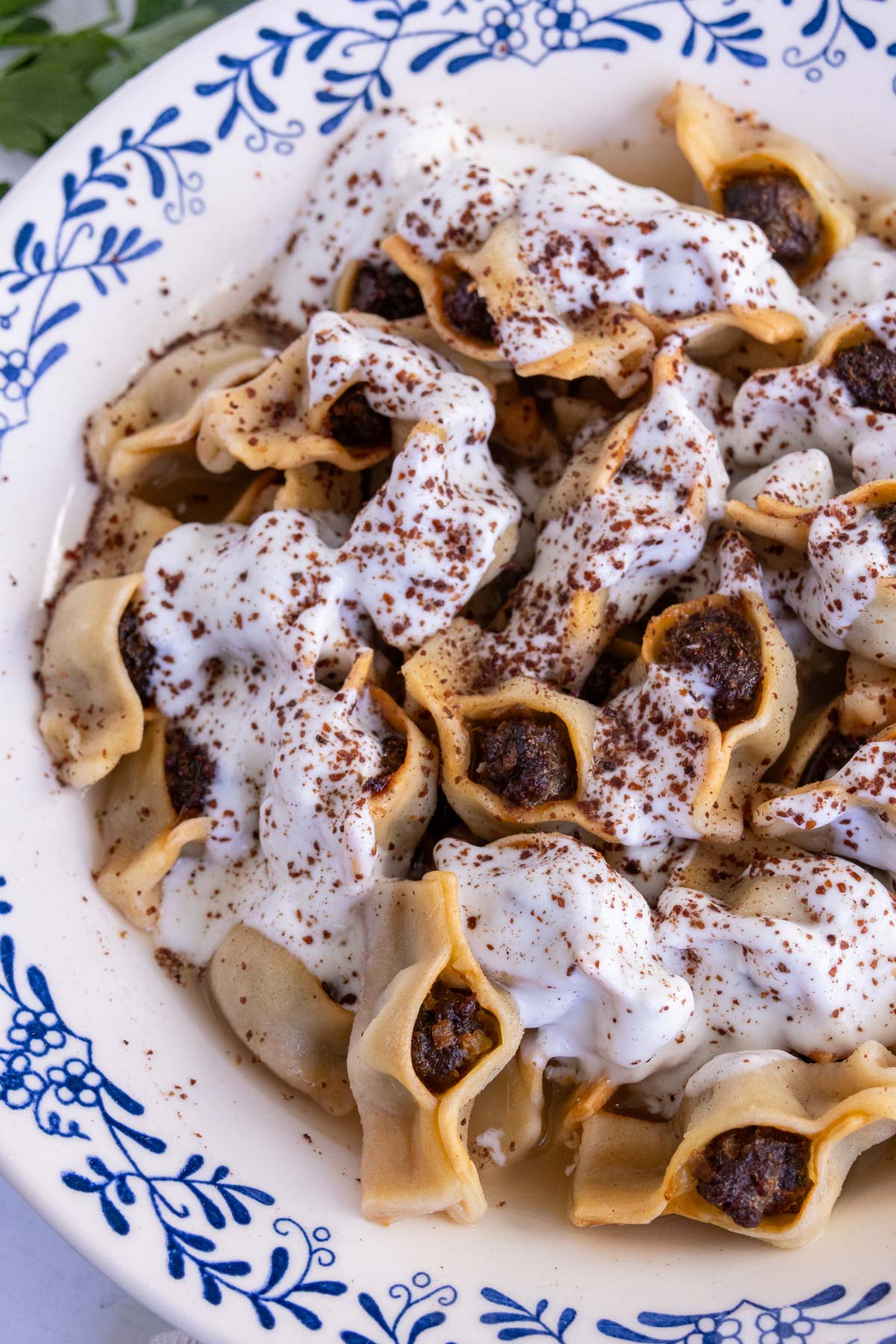 A bowl of Armenian manti topped with yogurt garlic sauce and ground sumac.