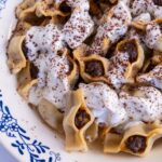 A bowl of Armenian manti topped with yogurt garlic sauce and ground sumac.