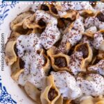 A bowl of Armenian manti topped with yogurt garlic sauce and ground sumac.