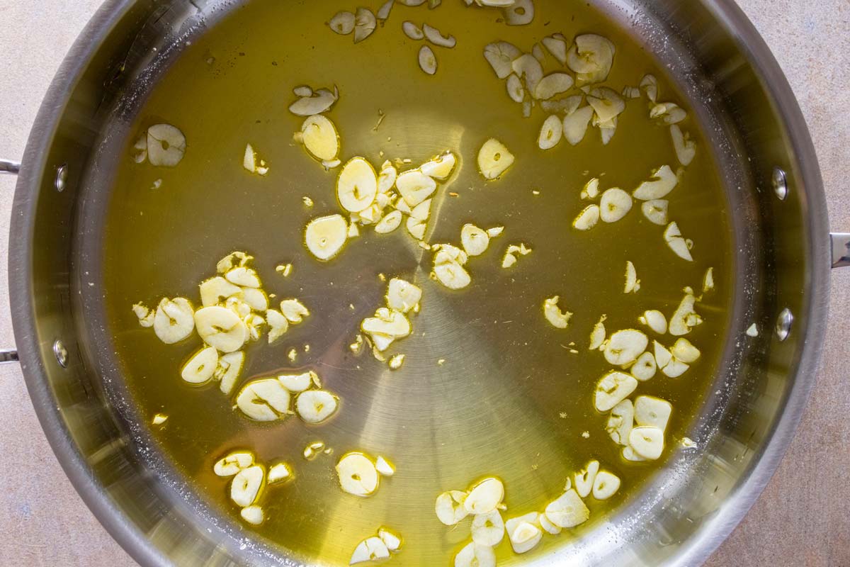 Thinly sliced garlic cooking in olive oil in a wide deep skillet.