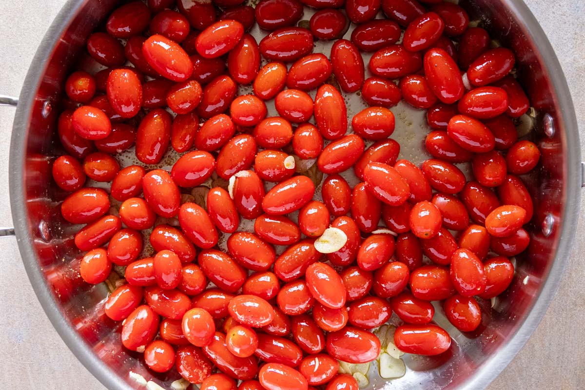 Grape tomatoes added to a skillet of thinly sliced garlic and olive oil.