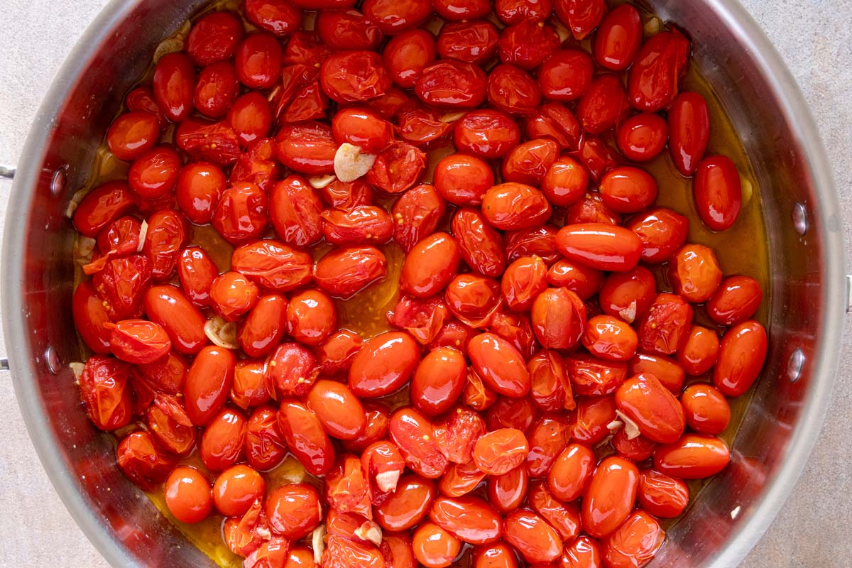 Grape tomatoes starting to burst after cooking in a skillet with sliced garlic and olive oil.
