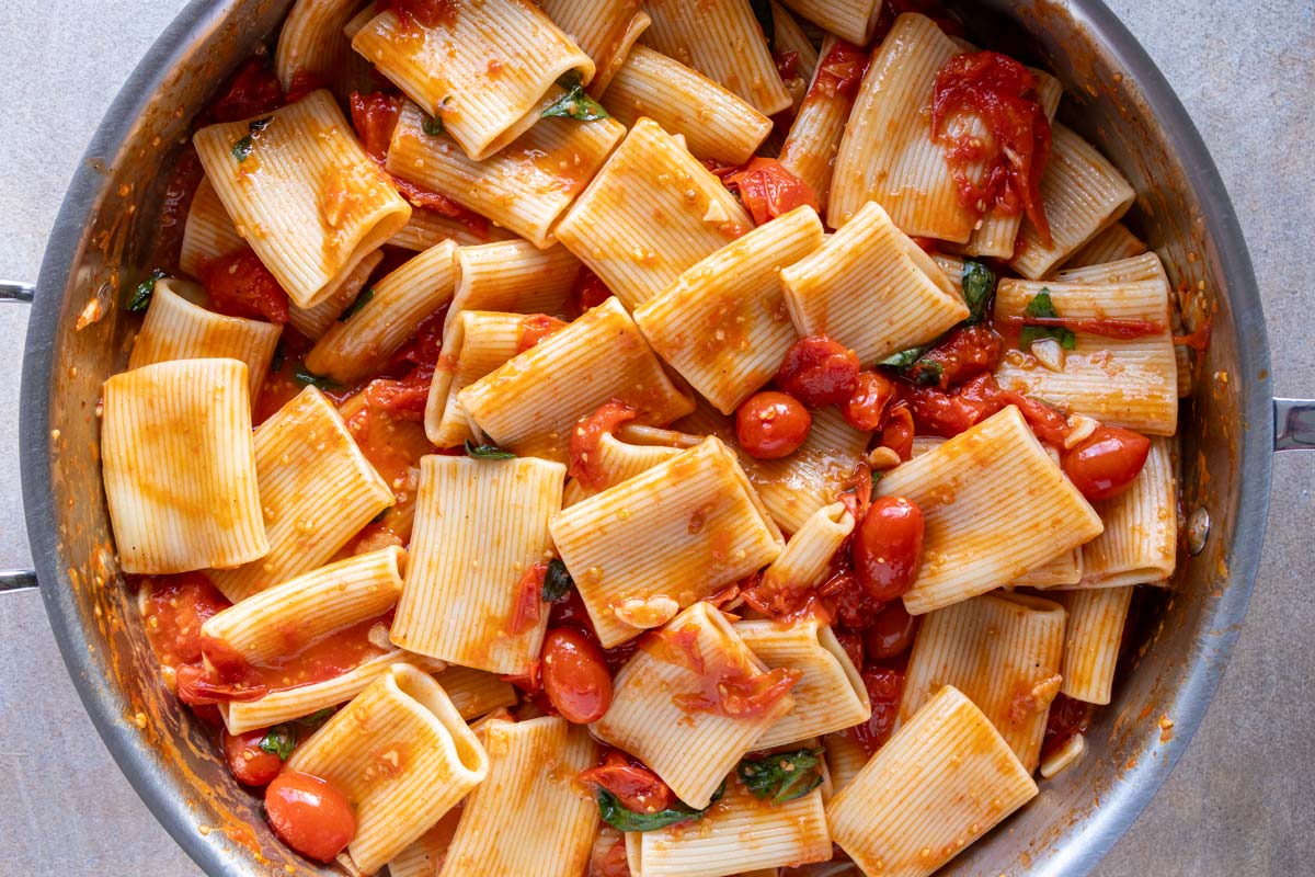 Paccheri pasta cooked in a deep skillet in a sauce of cherry tomatoes and basil.