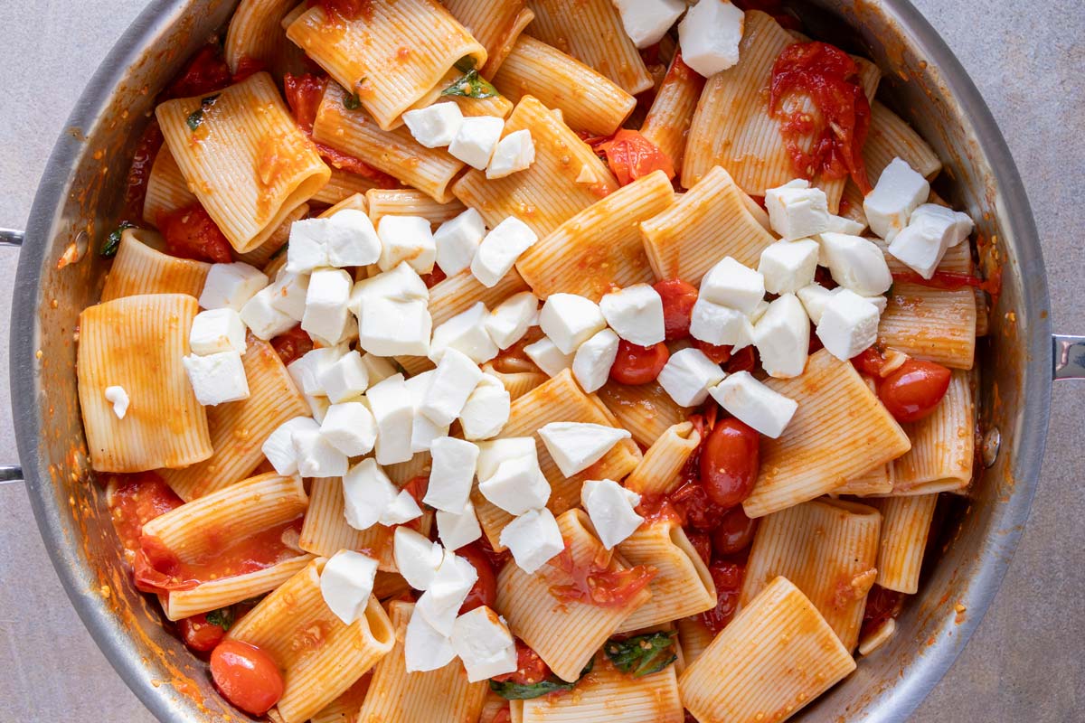 Cubed fresh mozzarella cheese added to a skillet of paccheri pasta in a cherry tomato sauce.