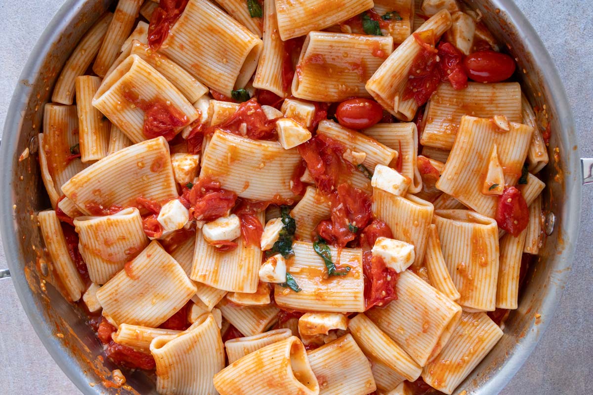 Cubed fresh mozzarella cheese stirred into a skillet of paccheri pasta in a cherry tomato sauce.