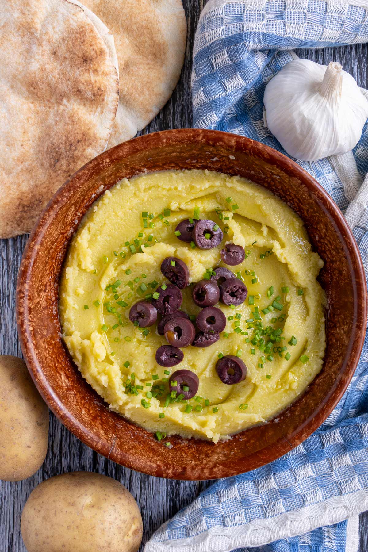 Greek skordalia dip served in a brown bowl with small pita breads on the side.