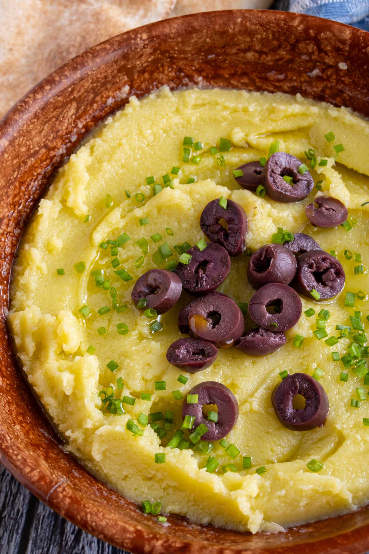 Creamy skordalia garlic and potato dip garnished with sliced olives and chives.