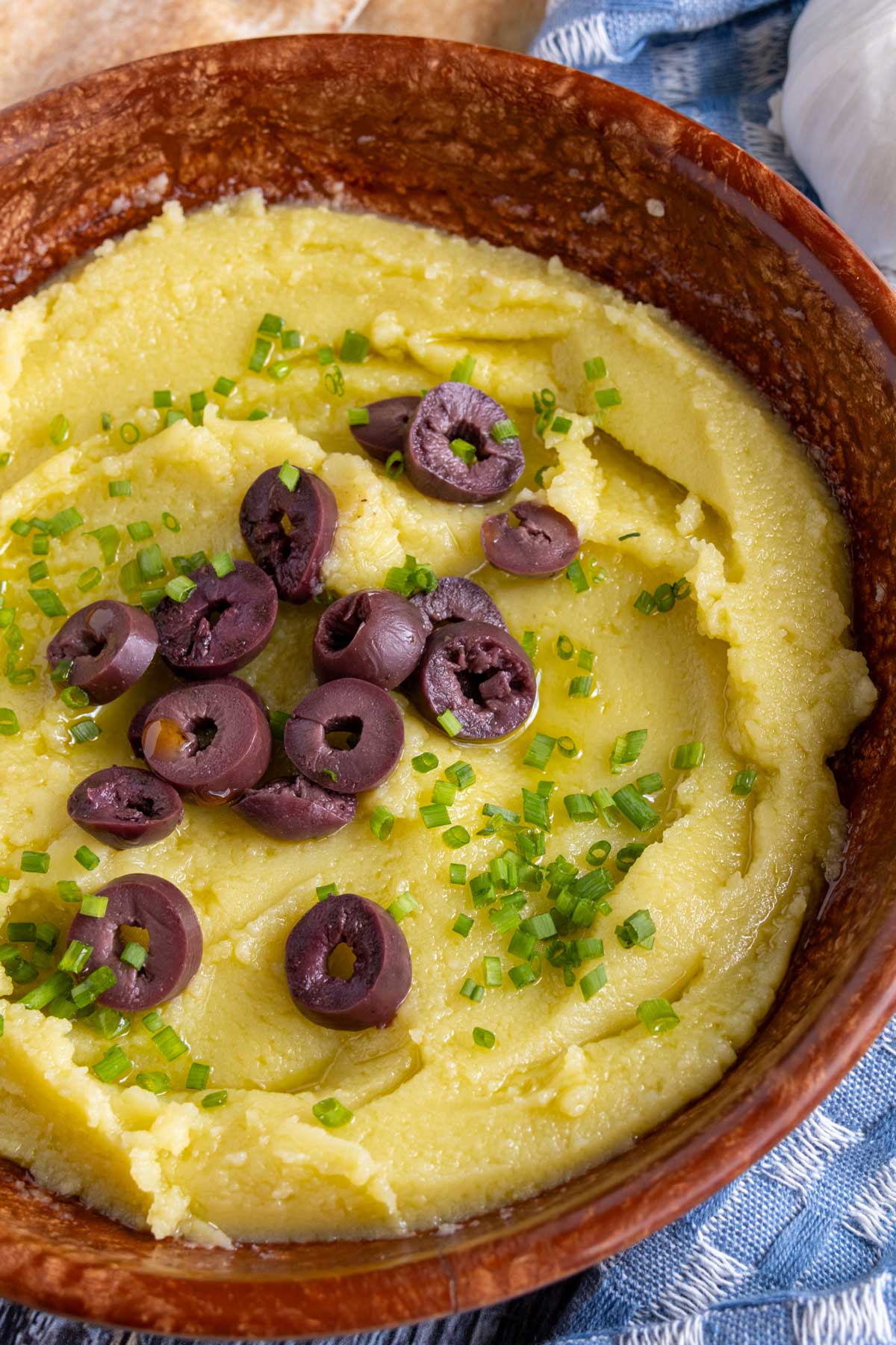 Skordalia garlic and potato dip served in a brown bowl topped with chives and sliced olives.