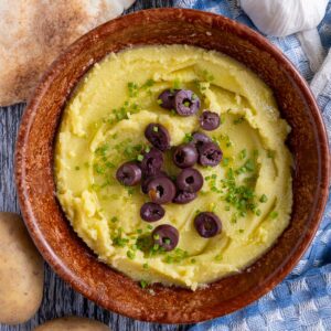 Greek skordalia dip served in a brown bowl with small pita breads on the side.