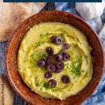 Greek garlic and potato spread (skordalia) topped with olives and chives in a brown bowl.