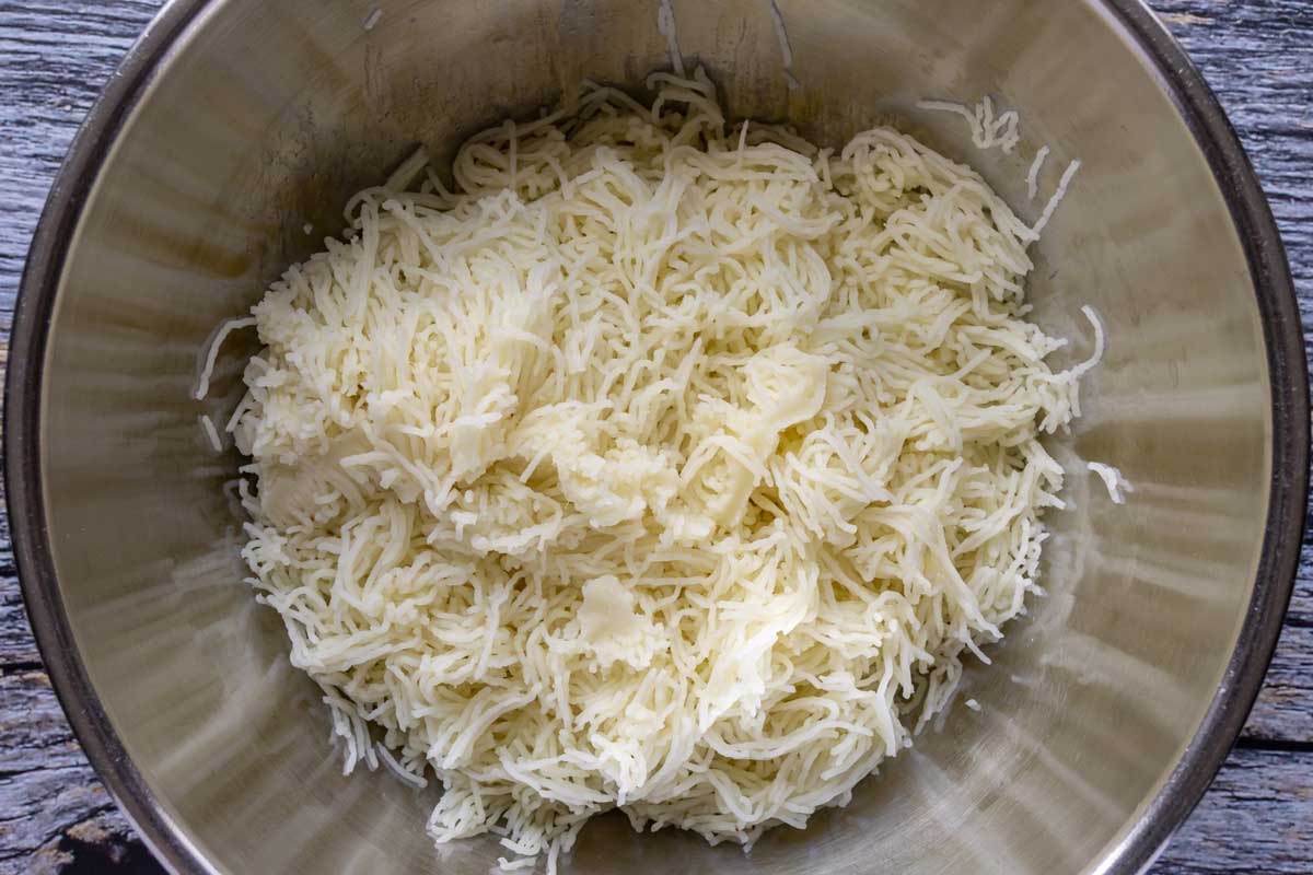 Boiled potatoes processed through a food mill into a metal mixing bowl.