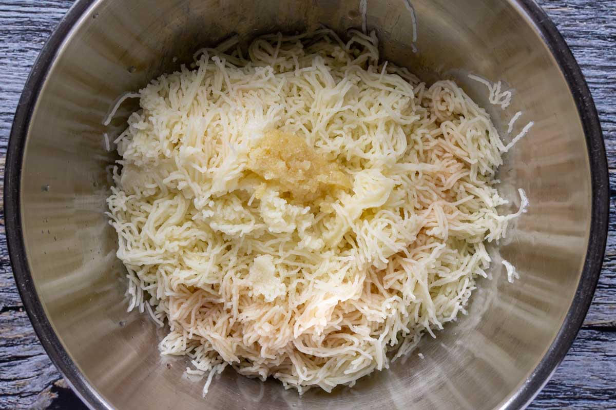 Lemon juice, red wine vinegar, and crushed garlic added to a bowl of processed boiled potatoes.