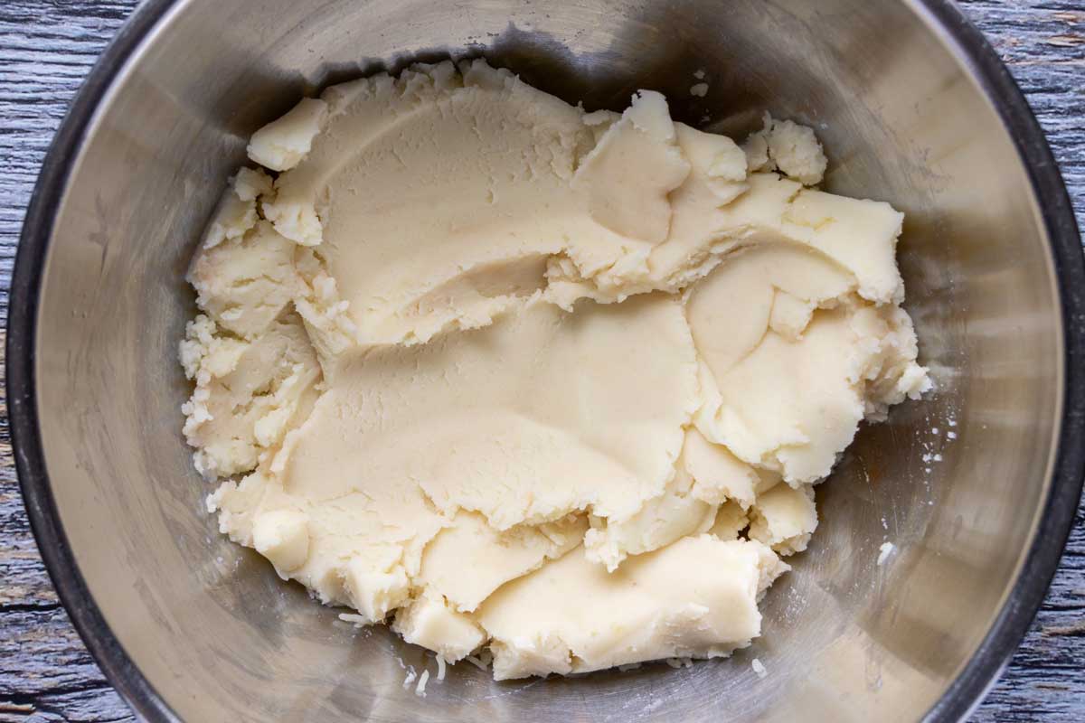 A thick mixture of mashed potatoes in a metal bowl.