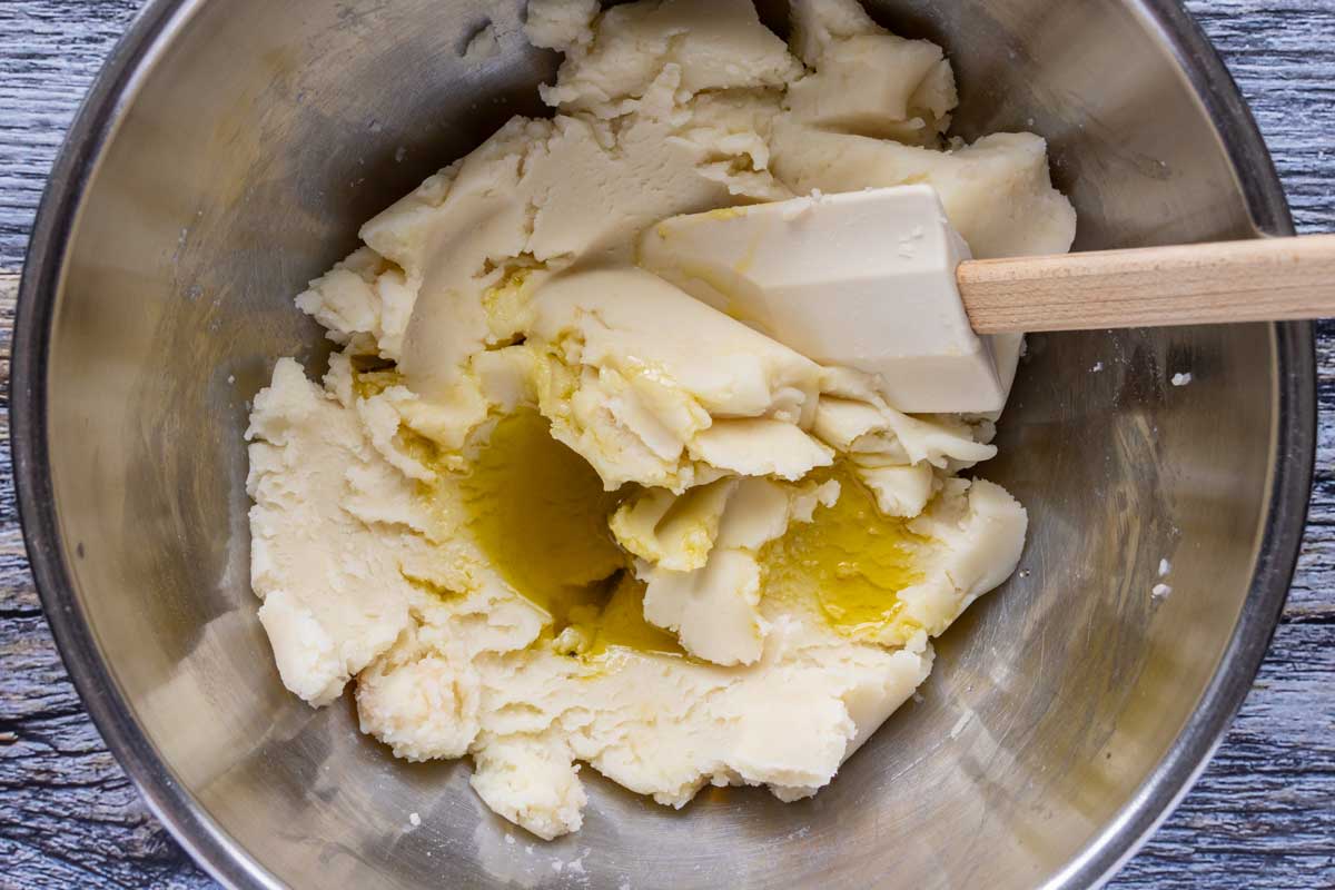 Adding extra-virgin olive oil to a bowl of thick mashed potatoes.