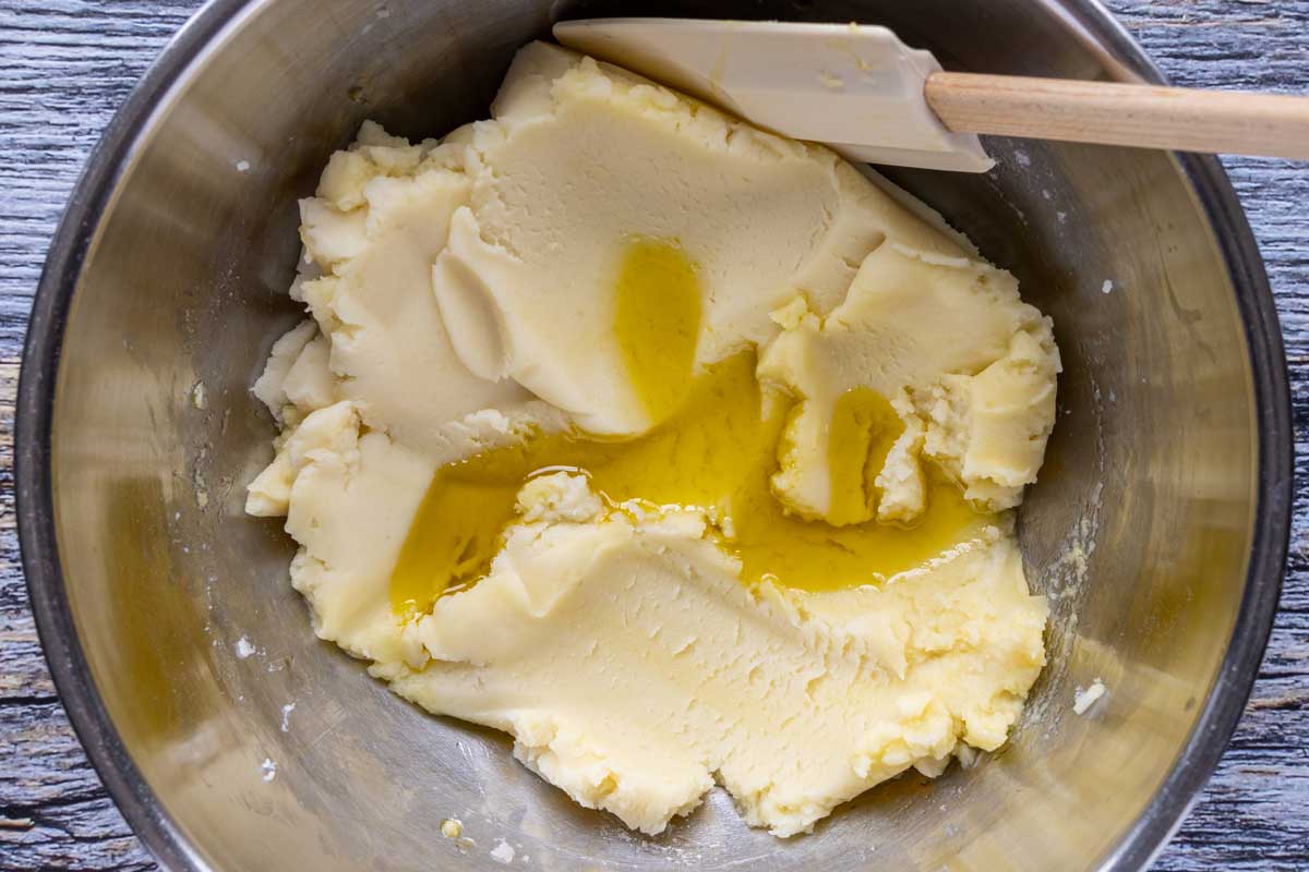 Adding more extra-virgin olive oil to a bowl of thick mashed potatoes.
