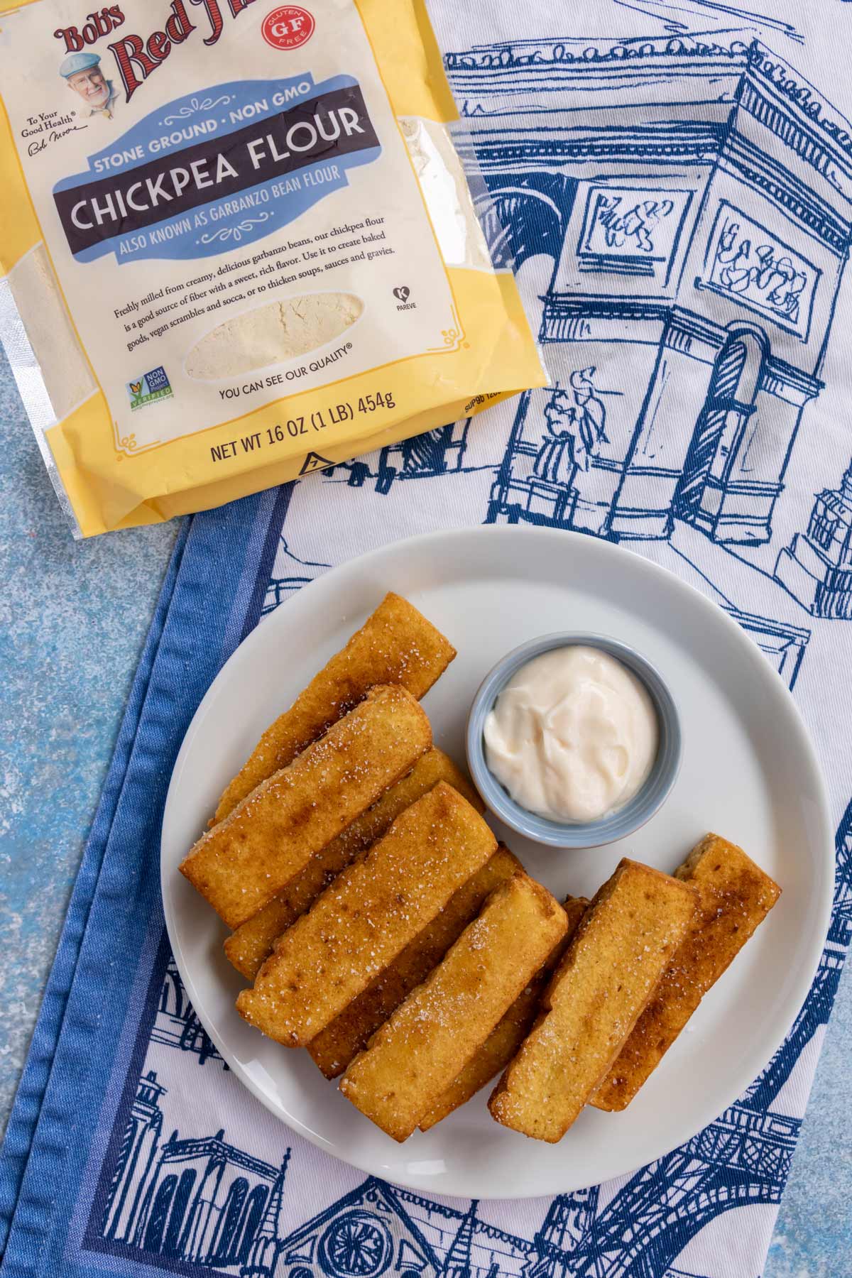 A plate of panisses with a side of aioli on a French-themed tea towel.
