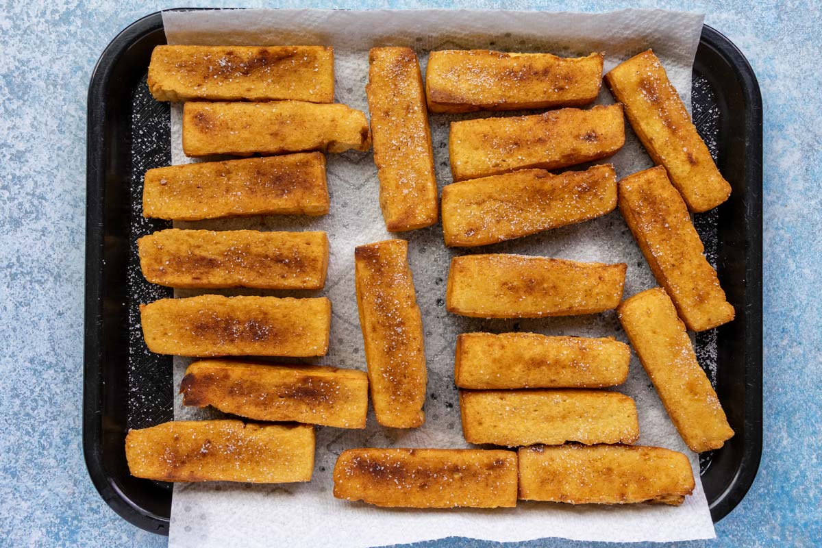 Fried panisses sprinkled with salt on a paper towel-lined cafeteria tray.