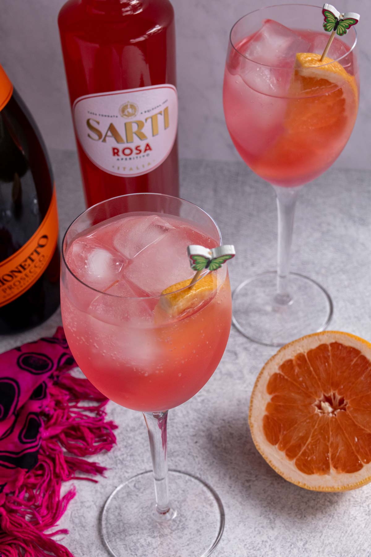 Two glasses of Sarti Spritz, each garnished with a half slice of grapefruit.