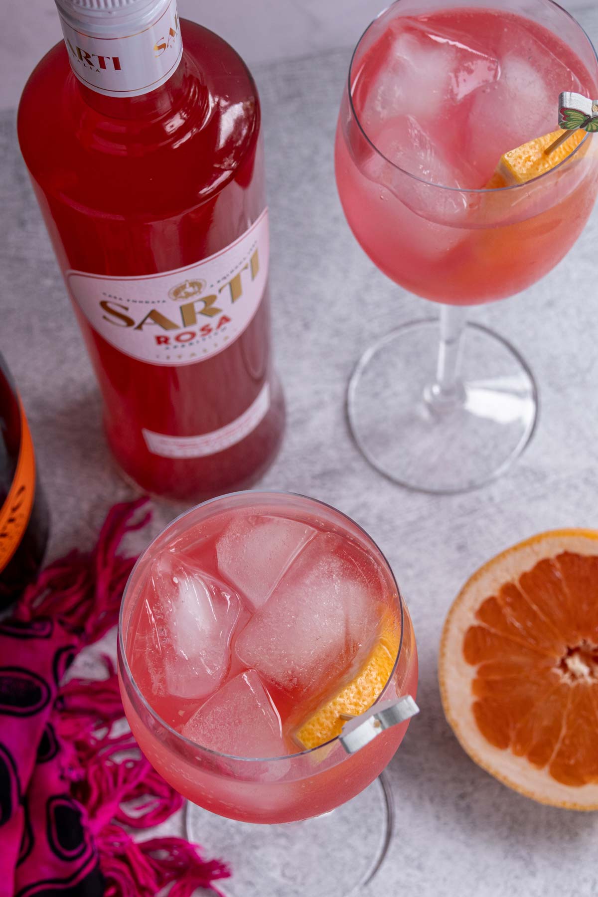 A bottle of Sarti Rosa, two glasses of Sarti Spritz, and half a grapefruit.