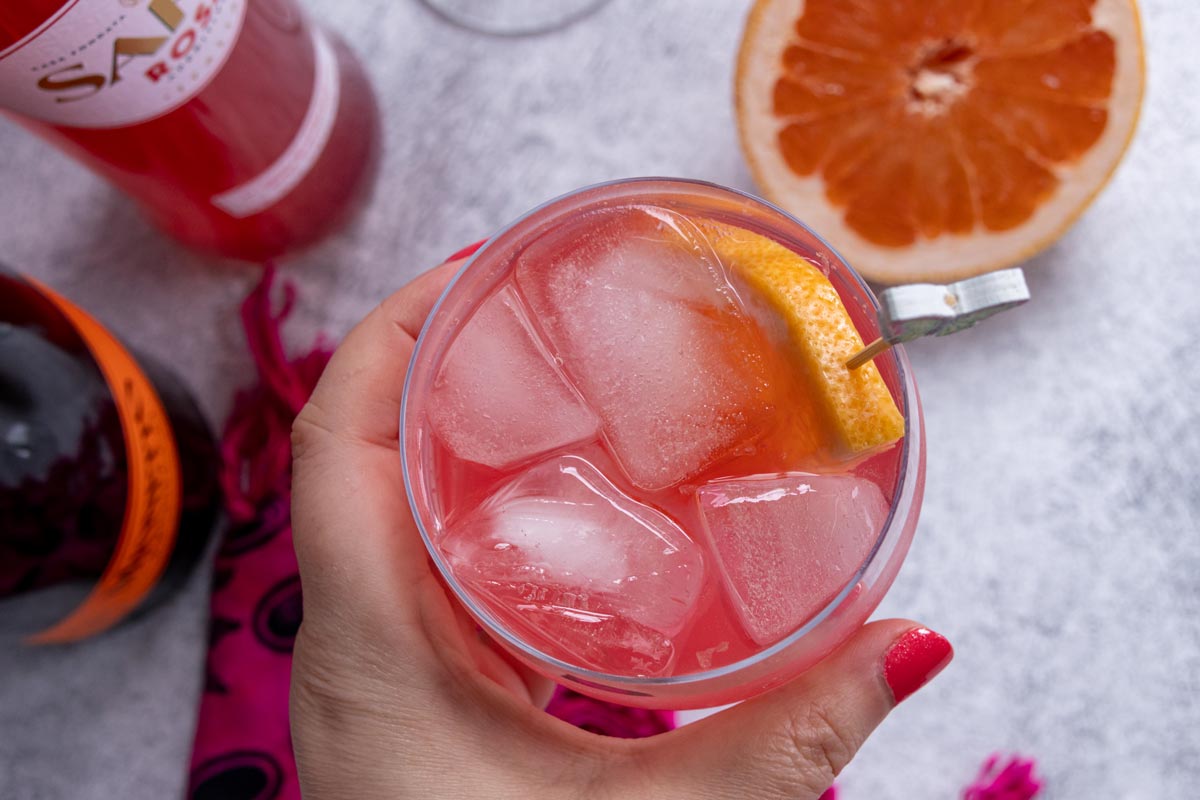 A hand holding a glass of Sarti Spritz garnished with a half slice of grapefruit.