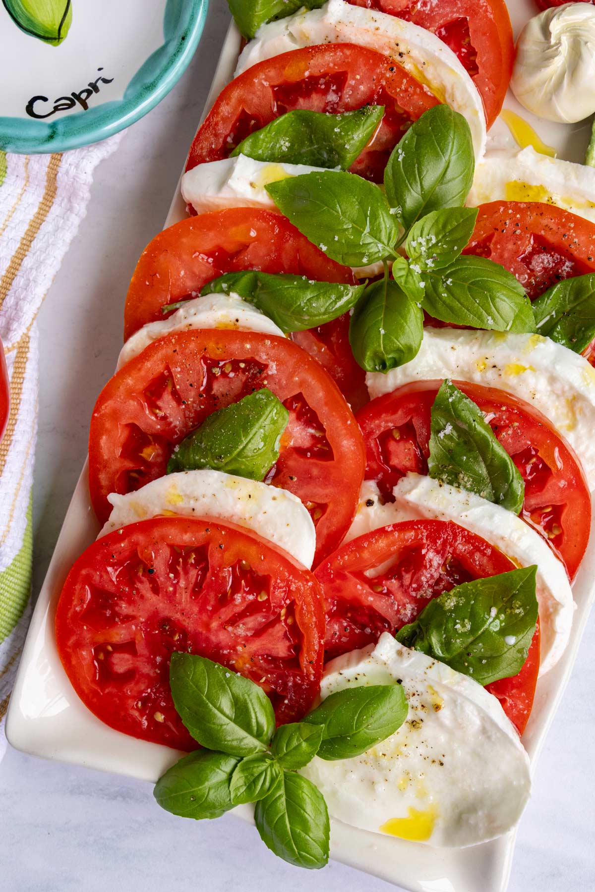 Slices of tomato, fresh mozzarella, and fresh basil leaves arranged on a rectangular platter.