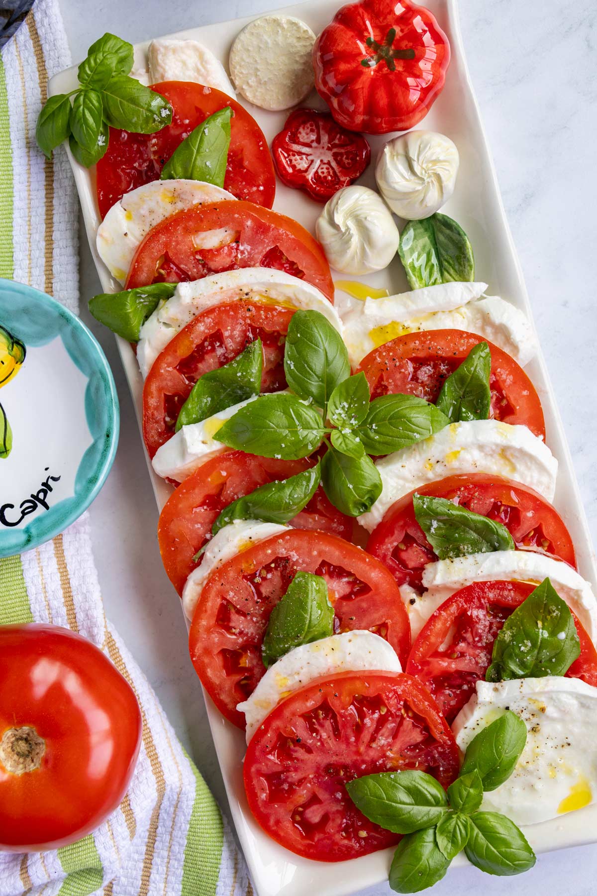 Caprese salad served on a rectangular platter with porcelain tomato, mozzarella, and basil on it.