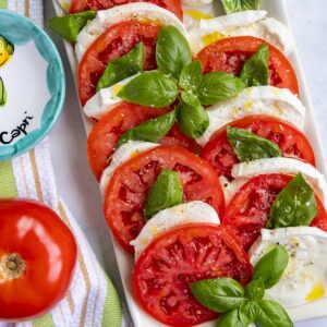 A platter of authentic caprese salad made with sliced tomatoes, buffalo mozzarella and basil.