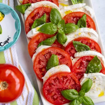 A platter of authentic caprese salad made with sliced tomatoes, buffalo mozzarella and basil.