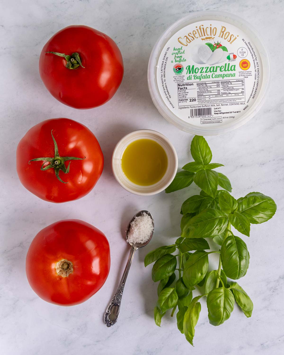Ingredients for authentic caprese salad on a white marble background.