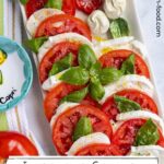 Caprese salad served on a rectangular platter with porcelain tomato, mozzarella, and basil on it.