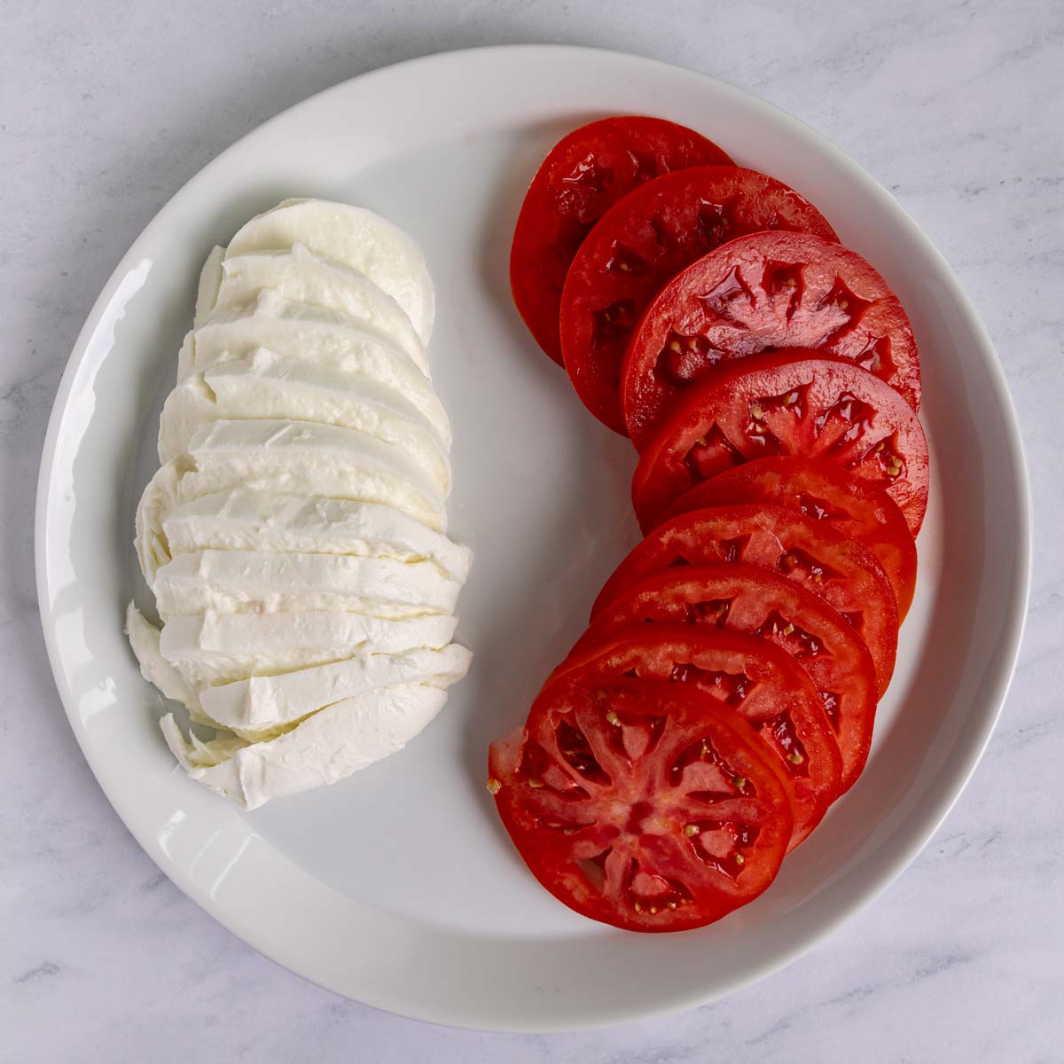 Sliced buffalo mozzarella and sliced beefsteak tomatoes fanned out on a white plate.