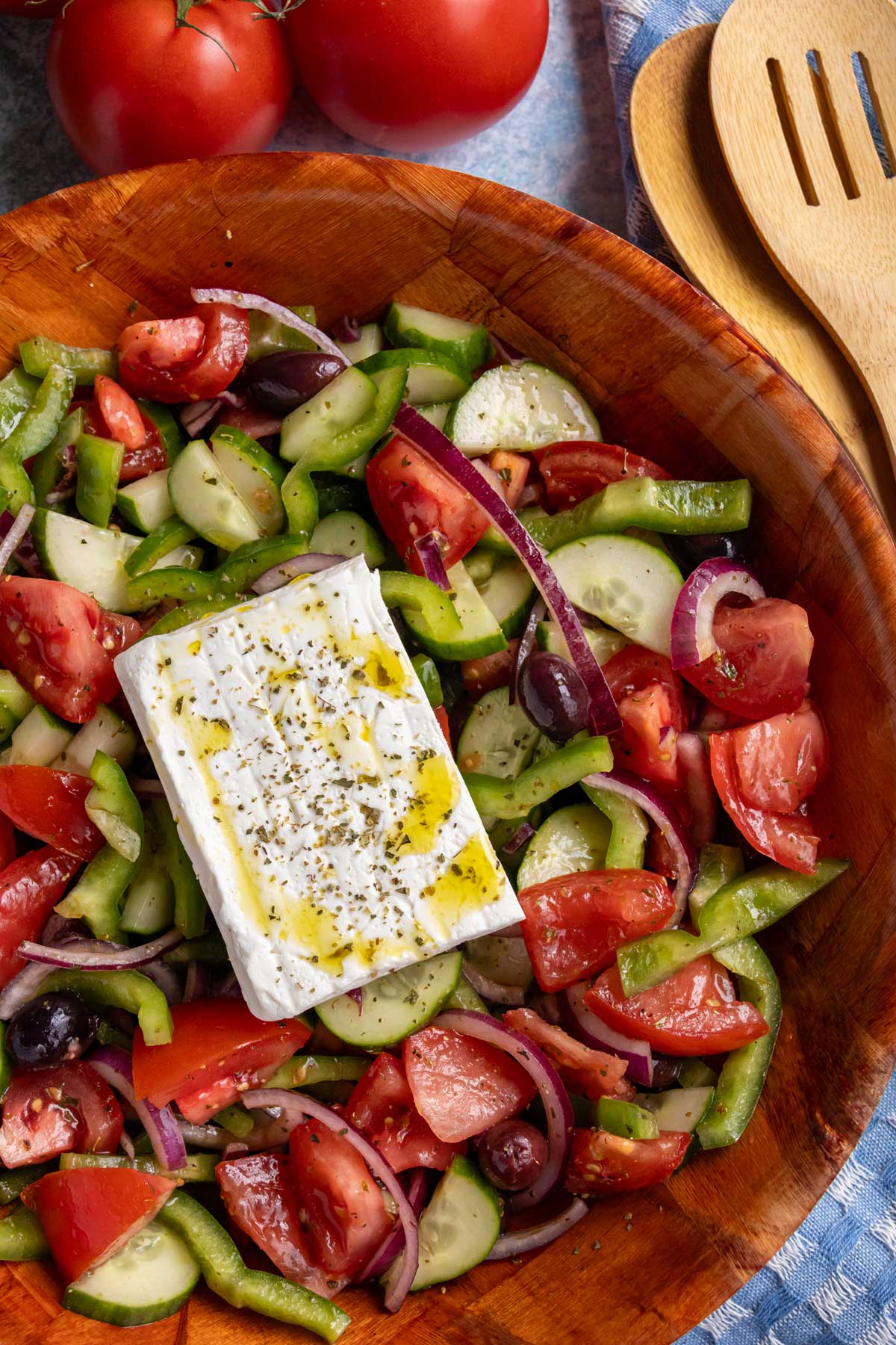 Greek salad in a woven wood salad bowl topped with a slab of feta cheese.