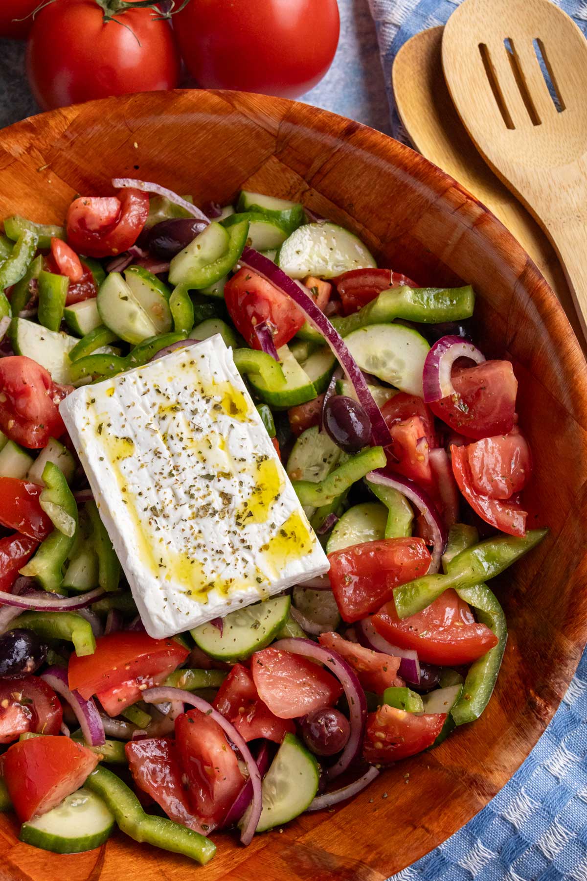 Greek salad topped with a slab of feta cheese garnished with oregano and olive oil.