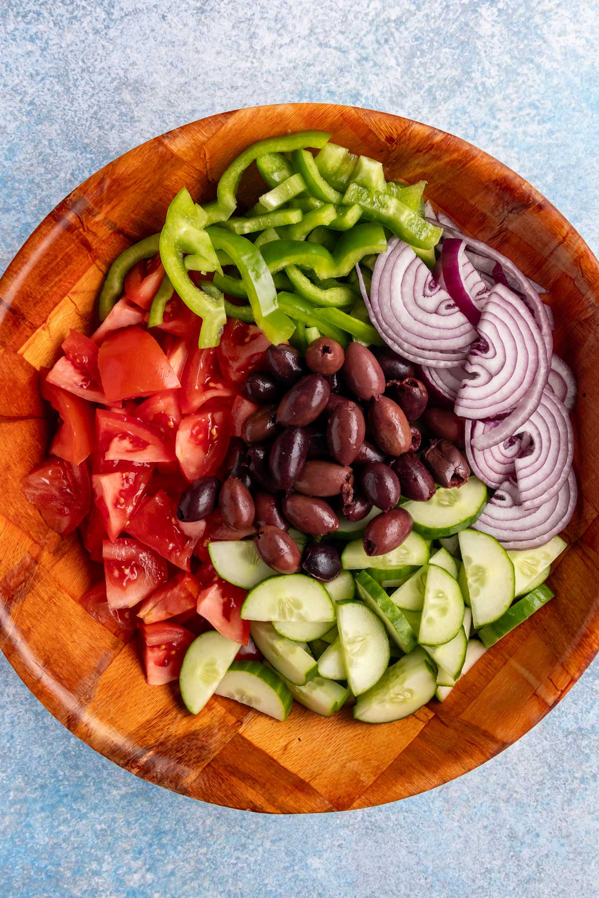 Sliced cucumber, red onion, green pepper, tomatoes, and kalamata olives in a salad bowl.