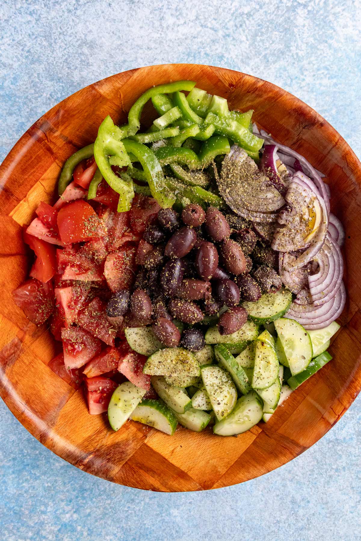 Sliced vegetables dressed with dried oregano, salt, pepper, olive oil, and vinegar before tossing.