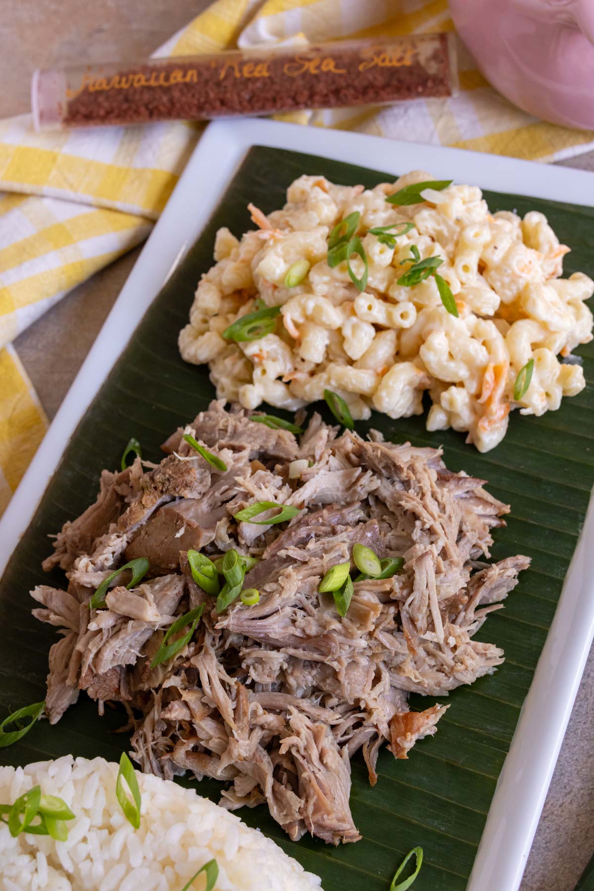 Shredded slow cooker kalua pork topped with sliced scallions served on a banana leaf.