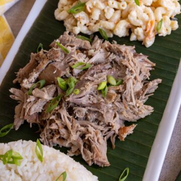 Shredded slow cooker kalua pork topped with sliced scallions served on a banana leaf.