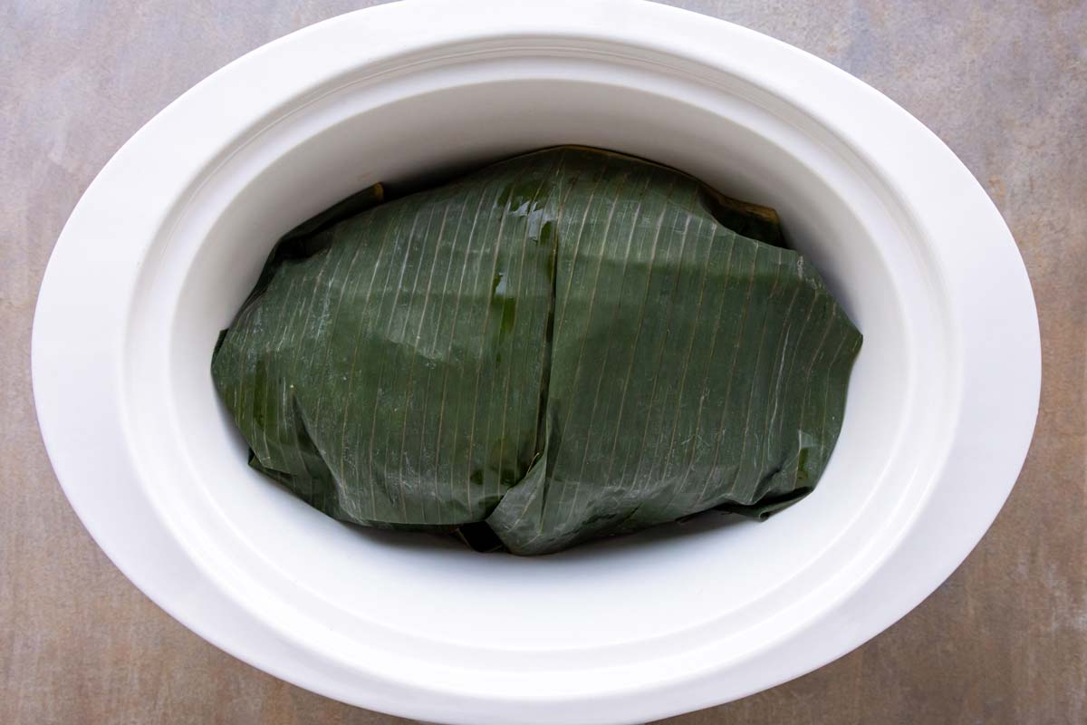 A banana leaf wrapped package in a slow cooker before cooking.