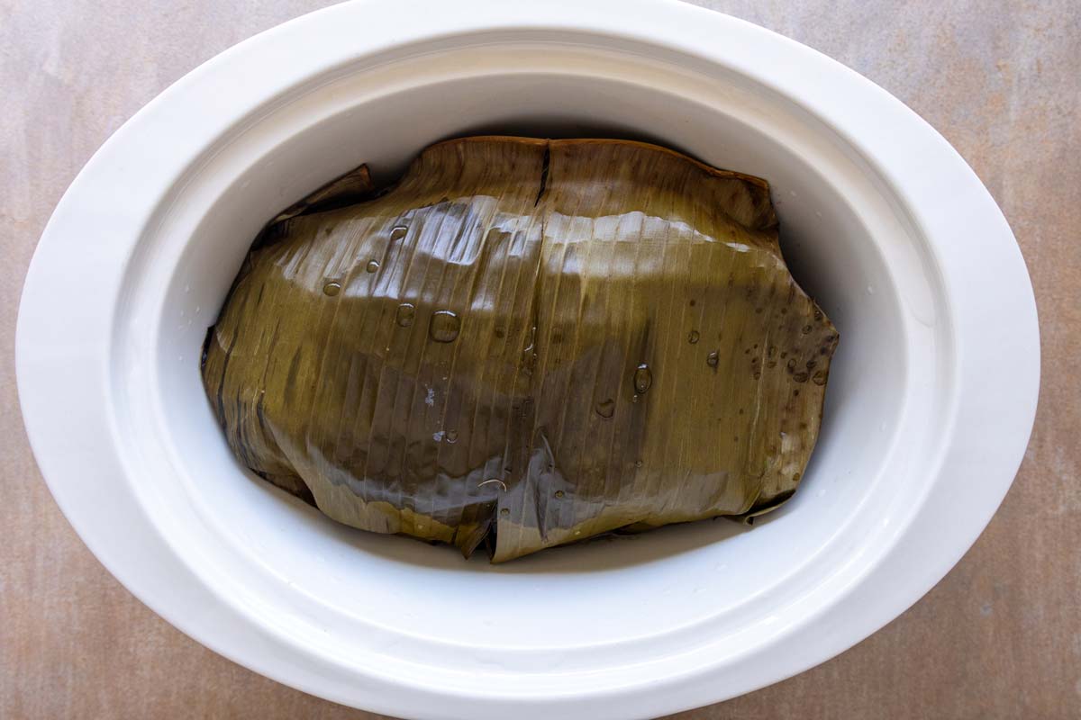 A banana leaf wrapped package in a slow cooker after cooking.