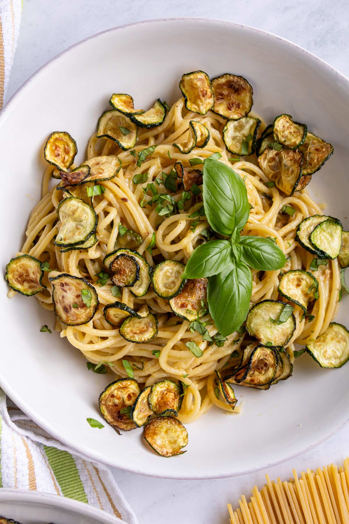 Spaghetti alla nerano topped with fried zucchini coins and a sprig of fresh basil.