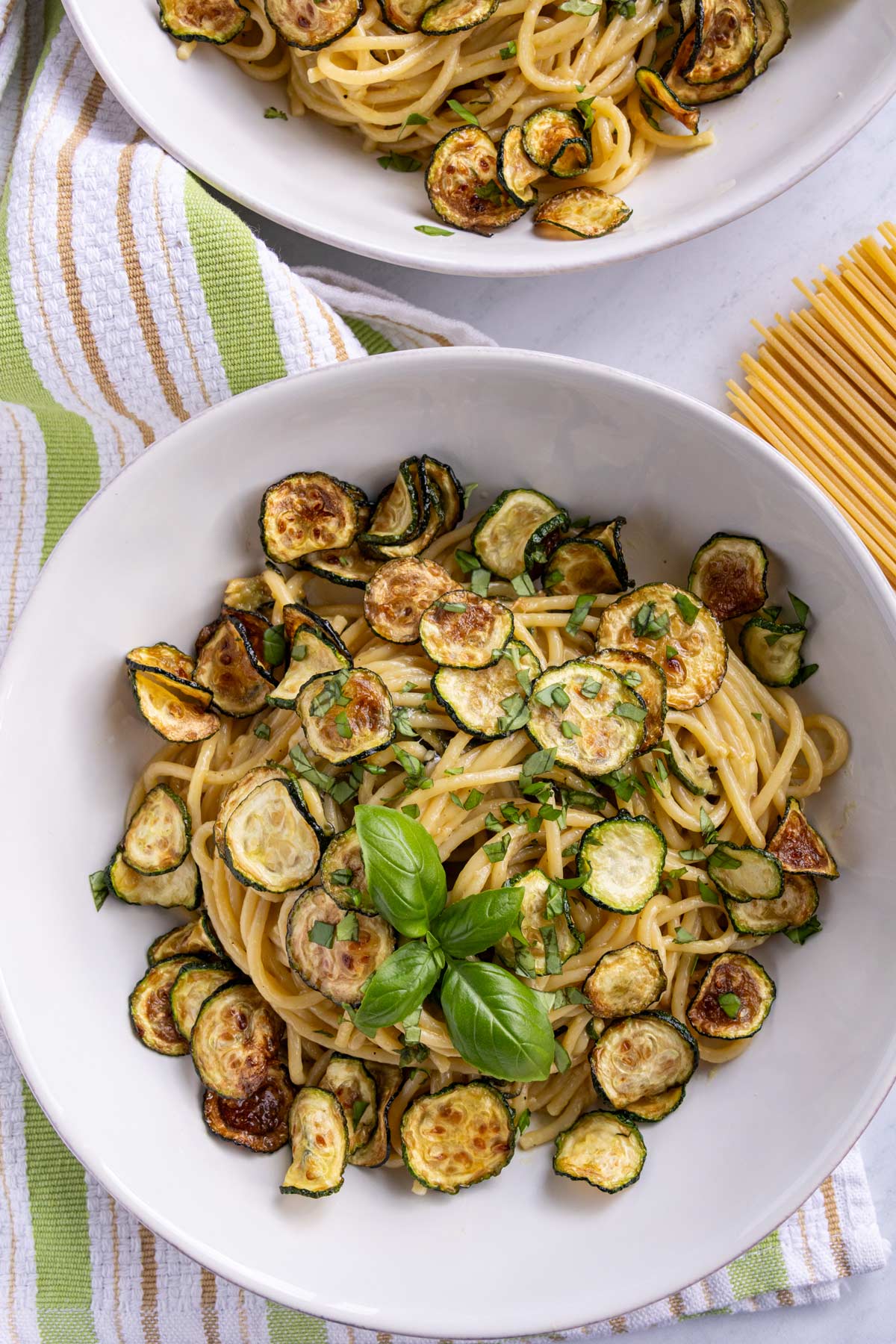 Cheesy spaghetti with fried zucchini coins topped with a spring of fresh basil.